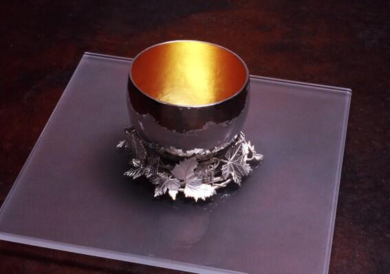 Silver cup /gold plated resting in a wreath of vine leaves on glass plate.